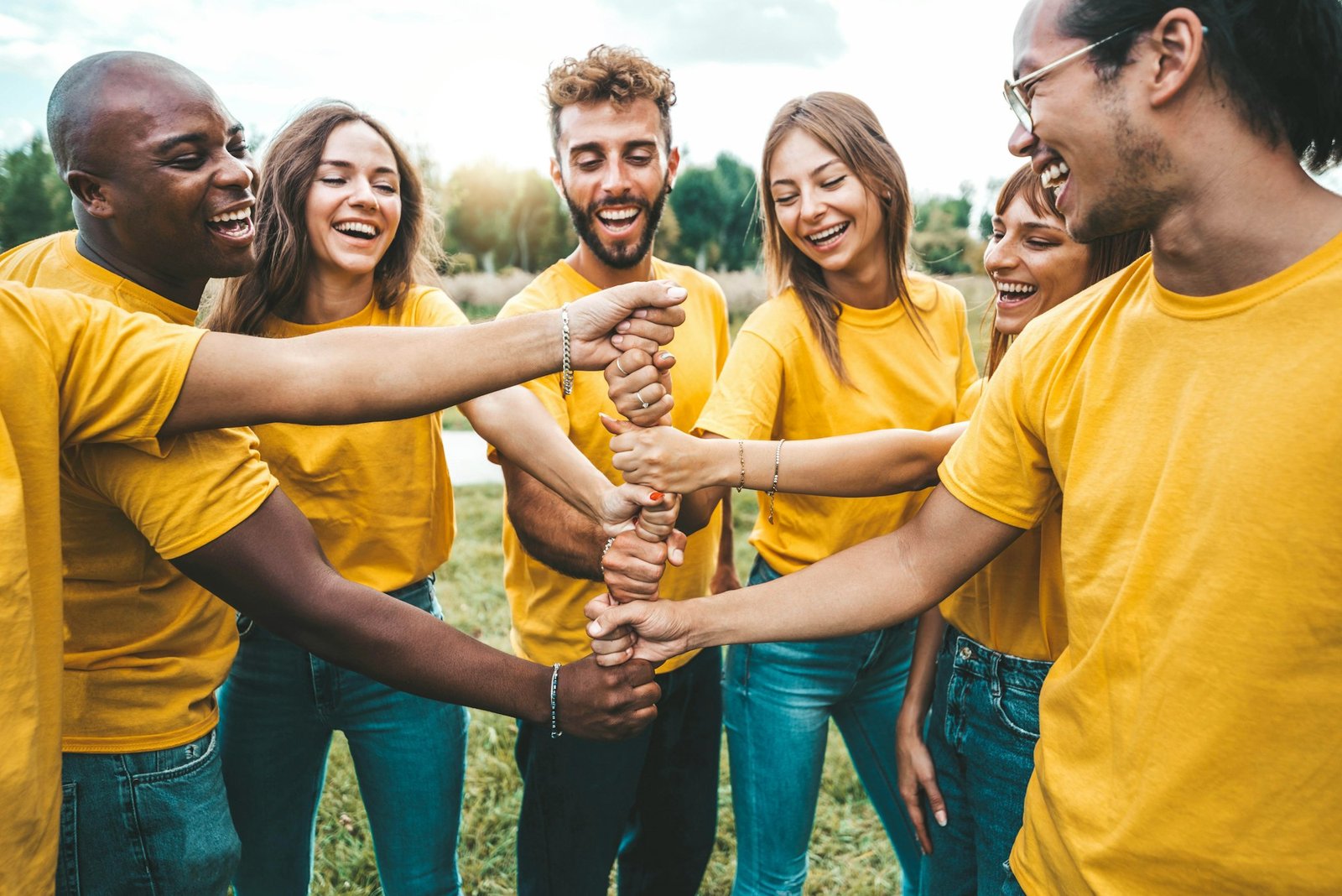 Multiracial happy young people stacking hands outside