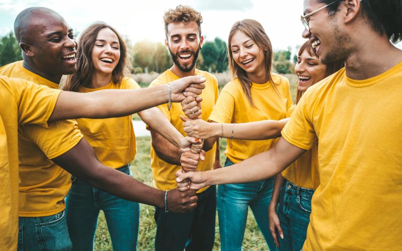 Multiracial happy young people stacking hands outside